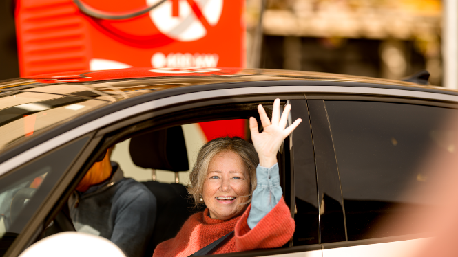 Bilde av dame som vinker mens hun kjører fra ladestasjon