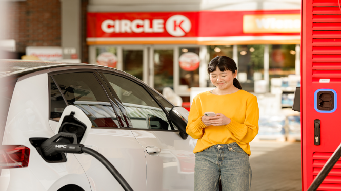 Bilde av dame som ser på mobilen mens hun lader bil