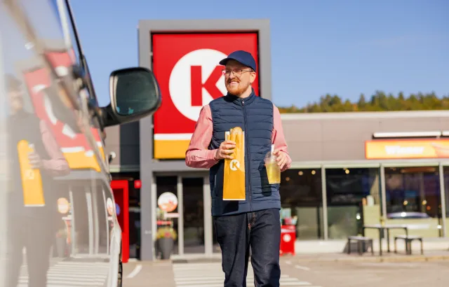 Man walking out of a Circle K store carrying a baguette and drink
