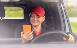 Bilde av fornøyd dame i bil med mobilen